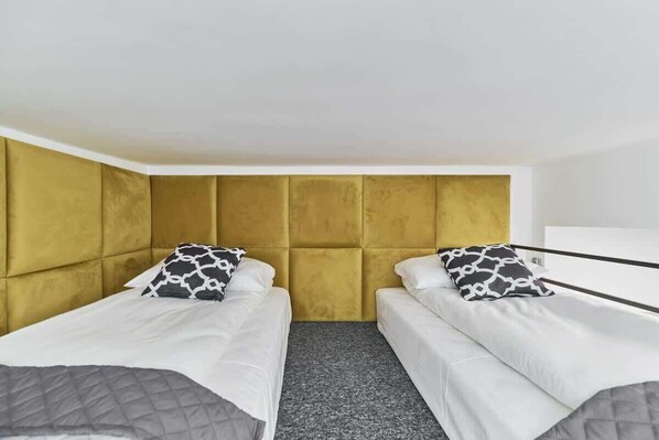 A room with two beds, a yellow headboard, and a grey carpet.
