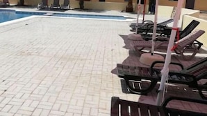Una piscina con sillas de descanso y sombrillas rojas.