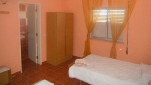 Una habitación pequeña con una cama individual, un armario, un televisor y una ventana con cortinas.
