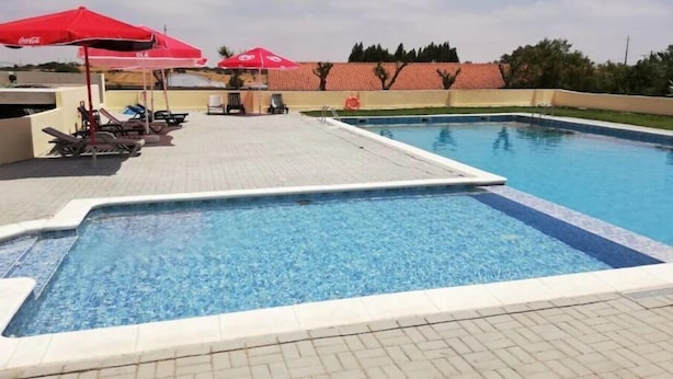 Una piscina con sillones de descanso y sombrillas rojas.
