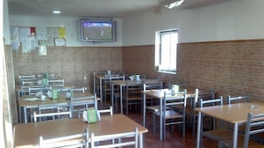 Un aula con escritorios y sillas dispuestas en filas, un televisor colgado en la pared y un ventanal que deja entrar luz natural.