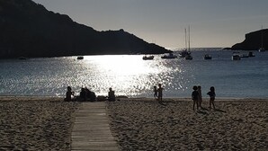 Une plage avec une promenade en bois menant à l’eau, des bateaux visibles au loin et des gens qui profitent du paysage.