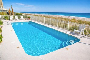 A rectangular pool with clear blue water, surrounded by a white fence, and overlooking a beach with a clear sky. - Ocean Shores 301 (North Myrtle Beach)