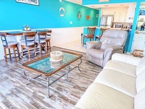 A living room with a blue wall, wooden chairs, a glass coffee table, and a beige sofa.