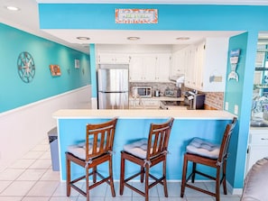 A kitchen with a blue accent wall, white cabinets, and a central island with bar stools. - Ocean Shores 301 (North Myrtle Beach)