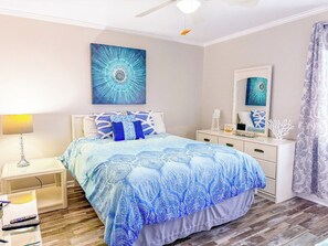 A bedroom with a bed, bedside table, nightstand, dresser, mirror, and a ceiling fan. - Ocean Shores 301 (North Myrtle Beach)