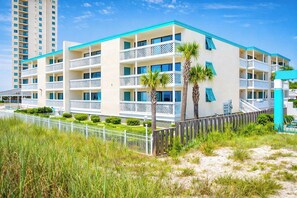 A multi-story hotel with balconies, a beach view, and a fenced garden area.