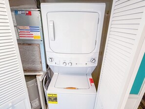A compact laundry room with a stacked washer and dryer, a control panel, and a visible energy efficiency label. - Ocean Shores 301 (North Myrtle Beach)