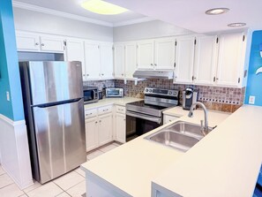 A modern kitchen with white cabinets, stainless steel appliances, and a large island with a sink. - Ocean Shores 301 (North Myrtle Beach)