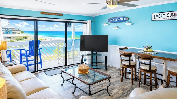 Una sala de estar con un televisor grande, un comedor con taburetes de bar y vista al océano.