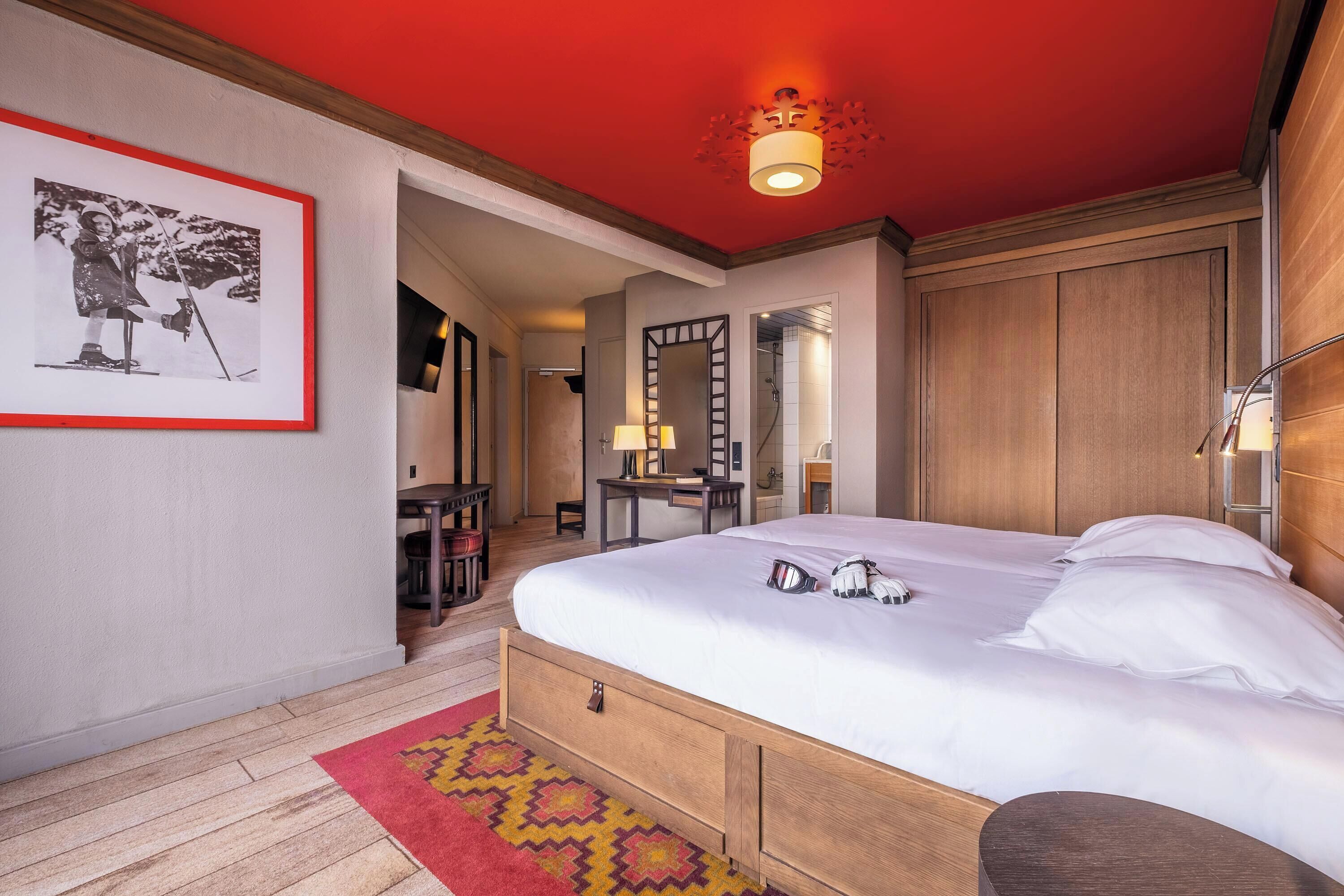A hotel room with a bed, a desk, a chair, a mirror, and a framed picture on the wall.