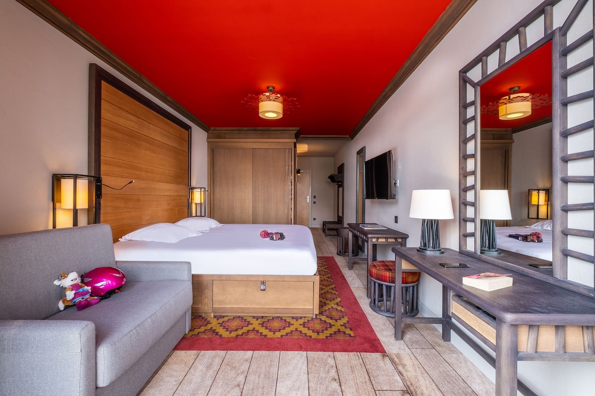 A hotel room with a bed, a sofa, a desk, and a mirror.