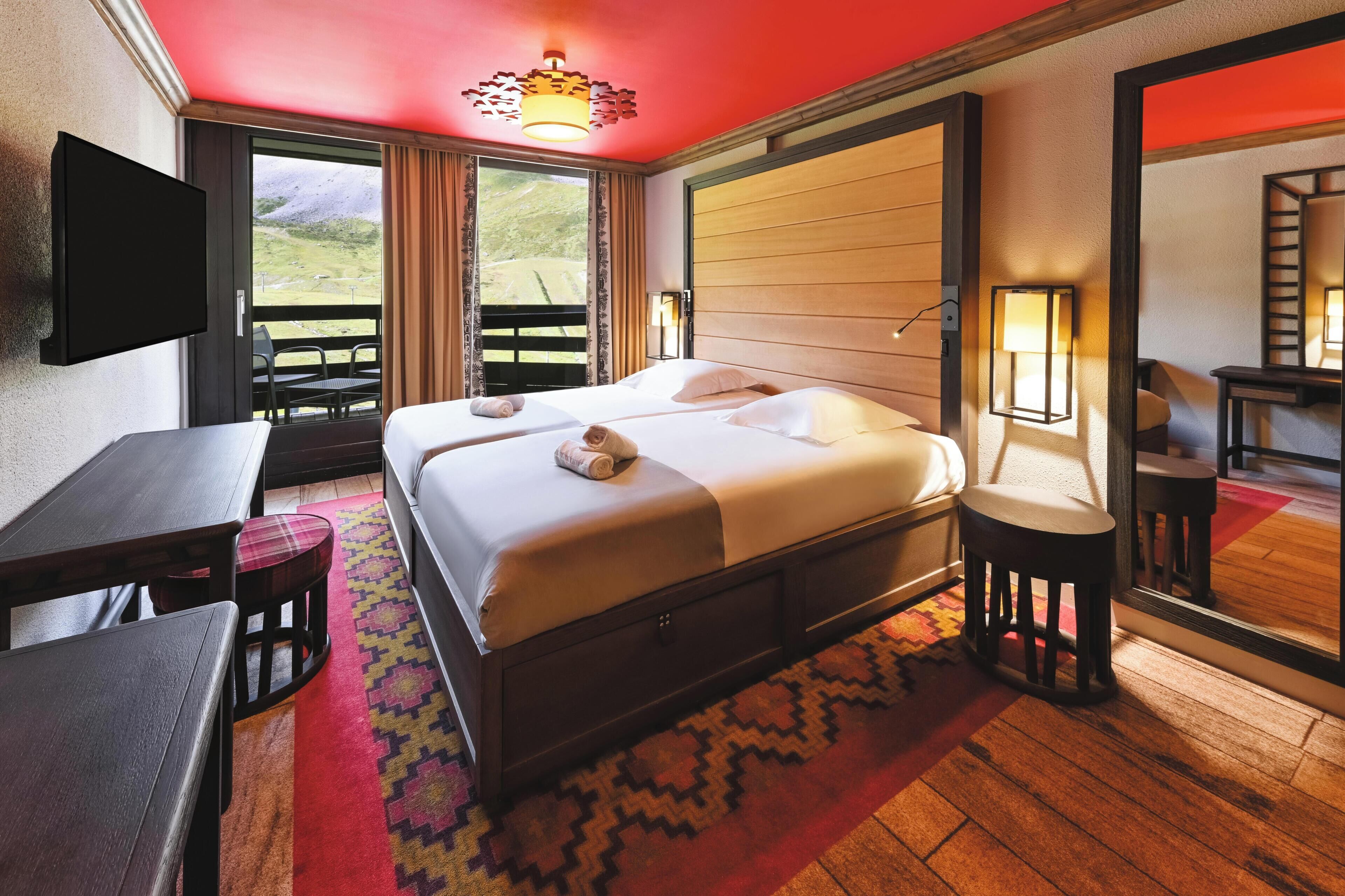 A hotel room with a bed, a desk, a chair, a TV, and a large window.
