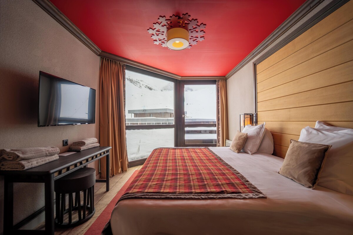 Habitación de hotel con cama, escritorio, televisión y ventana con vista a un paisaje nevado.