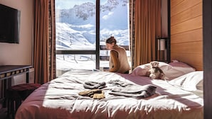 A hotel room with a bed, a window with curtains, a teddy bear, and a view of a snowy mountain. - Belambra Clubs Tignes - Val Claret (Tignes)