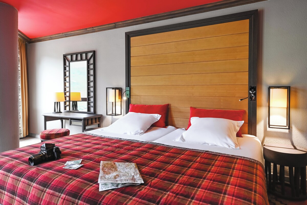Una habitación de hotel con una cama grande, dos lámparas de noche, un cabecero de madera y una colcha roja a cuadros.