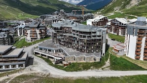 A modern hotel complex with multiple buildings, including a prominent multi-story structure with balconies, situated in a mountainous area with clear skies. - Belambra Clubs Tignes - Val Claret (Tignes)