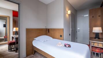 Habitación de hotel con cama de madera, una mesita con lámpara, espejo y una silla roja a cuadros.