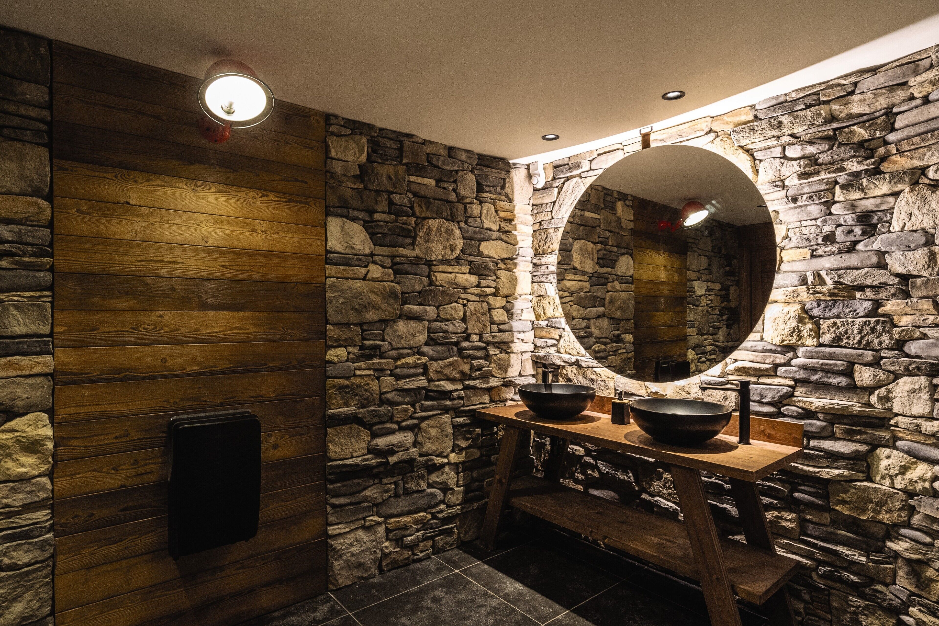 A rustic bathroom with stone walls, wooden paneling, and a wooden vanity with a bowl sink.