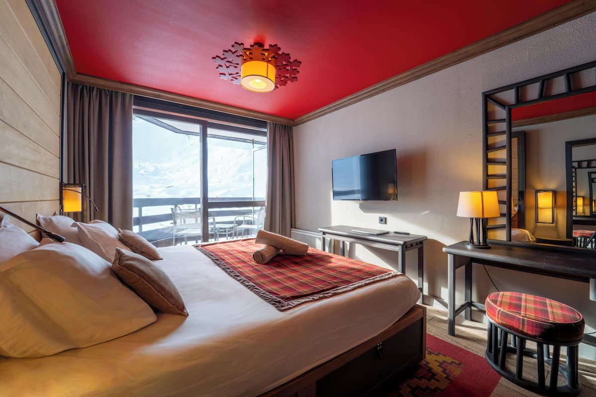 A hotel room with a large bed, a desk, a chair, a TV, and a window with curtains.