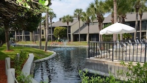 Un cortile d'hotel con una piccola fontana, palme e una zona piscina con lettini.