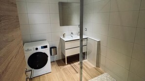 A modern bathroom with a glass shower enclosure, a built-in washing machine, and a vanity with a mirror. - RANDOM LISTING (Wintzenheim)