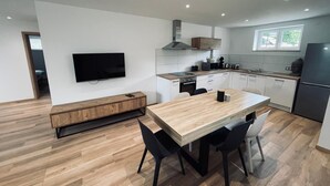 A modern kitchen with a wooden dining table, black chairs, a TV mounted on the wall, and a window providing natural light. - RANDOM LISTING (Wintzenheim)