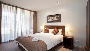 A hotel room with a large bed, two bedside lamps, a framed picture on the wall, and a window with curtains. - Resort Apartment 263 (TORQUAY)