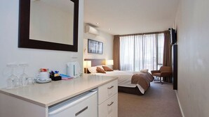 A hotel room with a bed, bedside tables, a desk, a chair, a large mirror, and a window with curtains. - Resort Hotel Room 261 (TORQUAY)