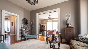 A spacious living room with a large mirror, a blue armchair, a patterned sofa, and a wooden cabinet. - Immersion Experience Into a Fictional Magical World (Saint Joseph)