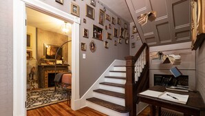 A staircase with a wooden handrail, a small table with books and a notebook, and a wall decorated with framed pictures. - Immersion Experience Into a Fictional Magical World (Saint Joseph)