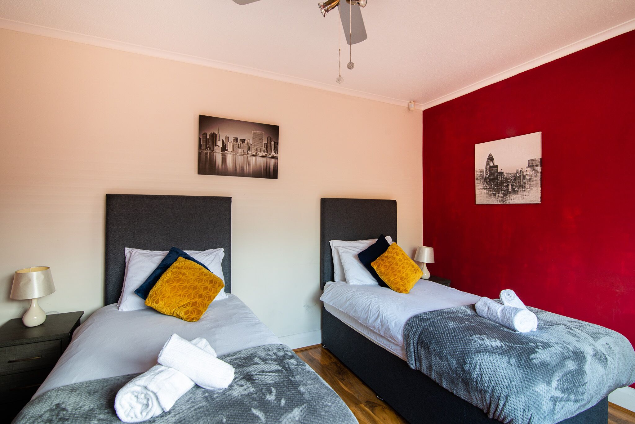 Een hotelkamer met twee bedden, elk voorzien van een hoofdbord, een rode accentmuur en kunstwerken met een stadsgezicht.