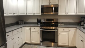 A modern kitchen with white cabinets, stainless steel appliances, and a granite countertop. - Centrally located in OakBluffs on Martha’s Vineyard (Oak Bluffs)