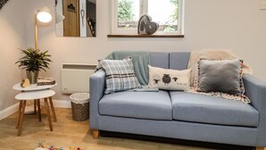A cozy living room with a blue sofa, a small round table, a potted plant, and a window with a view of greenery.