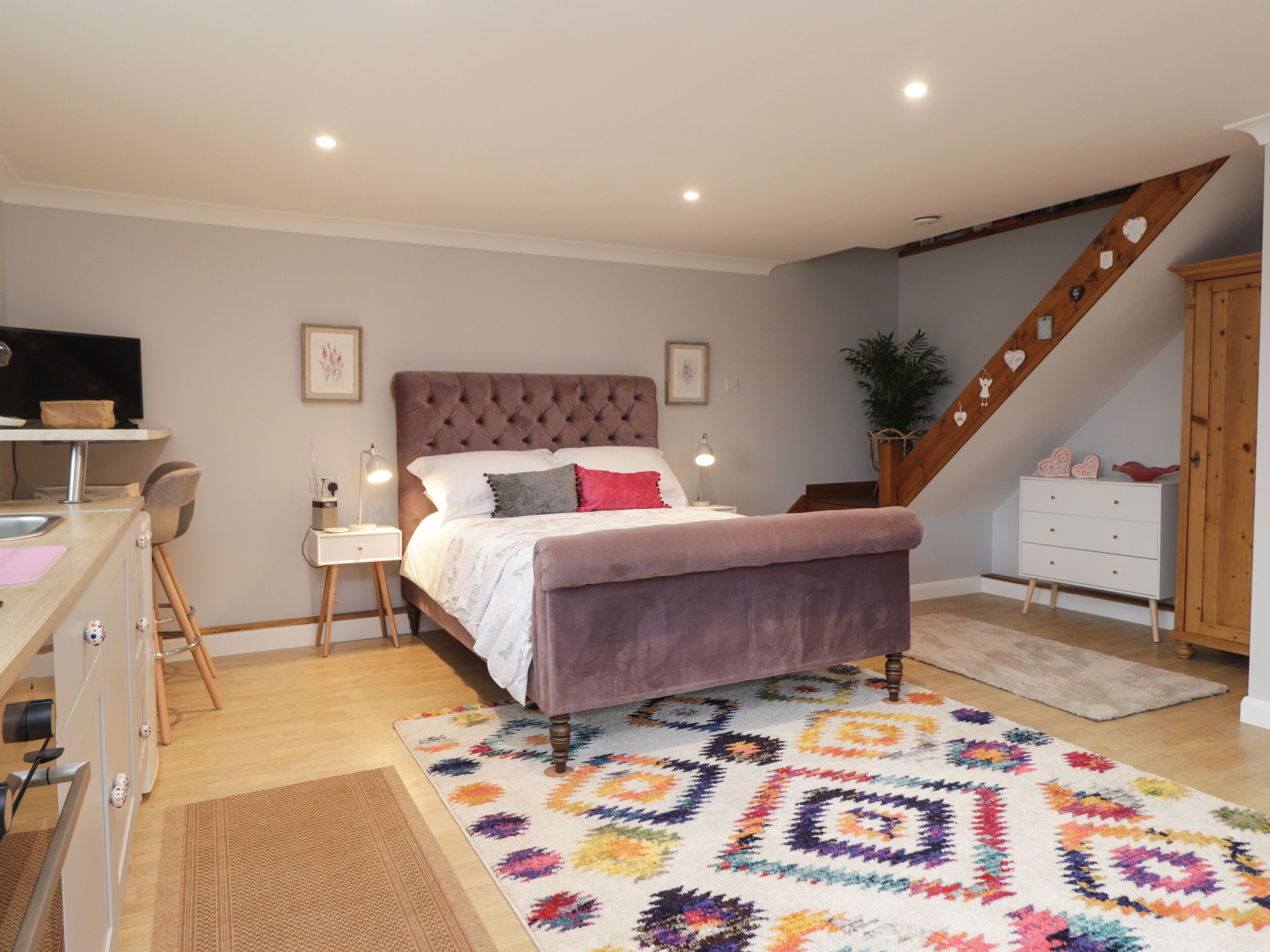A bedroom with a bed, bedside tables, a desk, a chair, a staircase, and a plant.