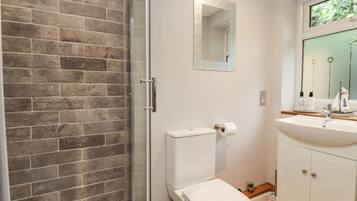 A bathroom with a glass shower enclosure, a white toilet, a sink with a mirror above it, and a window with a view of greenery.