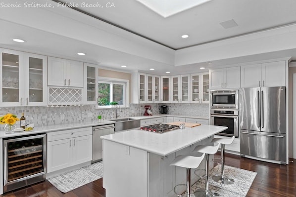 A modern kitchen with white cabinetry, stainless steel appliances, and a central island with bar stools.