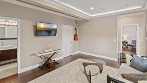 Ein großzügiges Wohnzimmer mit einem großen Fernseher, einem Klavier und einer Gitarre an der Wand.