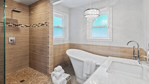 Un bagno moderno con una vasca da bagno freestanding, uno spazio doccia in vetro e un lampadario.