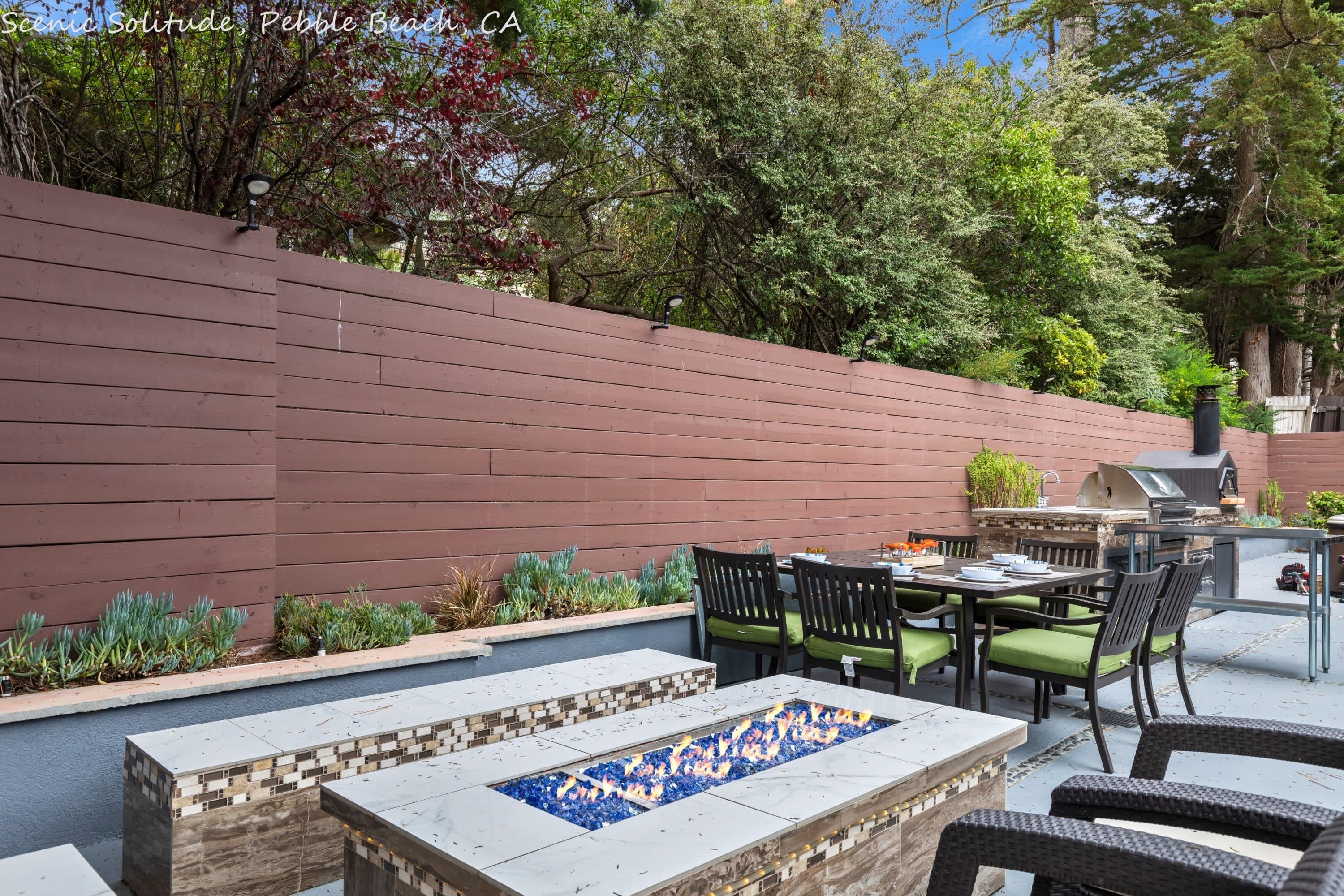 An outdoor patio with a fire feature, seating, and a grill area.