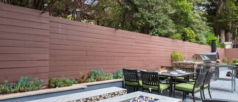 An outdoor patio with a fire feature, seating, and a grill area.