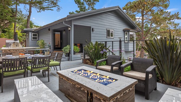 Ein Haus mit einer Terrasse, die Gartenmöbel, eine Feuerstelle und verschiedene Pflanzen umfasst.