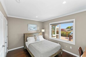 A bedroom with a bed, a window with a view of the outdoors, a painting on the wall, and a nightstand. - Shell's Treasure: Fully Updated Three bedroom home with Ocean Views (Pacific Grove)