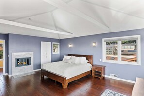 A bedroom with a bed, a fireplace, a nightstand, a window, and a view of the outside. - Shell's Treasure: Fully Updated Three bedroom home with Ocean Views (Pacific Grove)