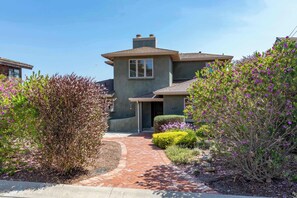 A residential house with a brick pathway leading to the entrance, surrounded by various shrubs and flowering plants. - Shell's Treasure: Fully Updated Three bedroom home with Ocean Views (Pacific Grove)