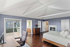 A bedroom with a bed, a desk, a chair, a dresser, a fireplace, and a sliding glass door to a balcony. - Shell's Treasure: Fully Updated Three bedroom home with Ocean Views (Pacific Grove)
