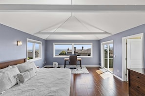 A bedroom with a bed, desk, and large windows overlooking a view.
