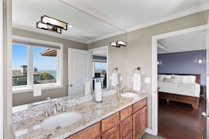 A bathroom with a double sink vanity, a large mirror, and a view of the ocean.
