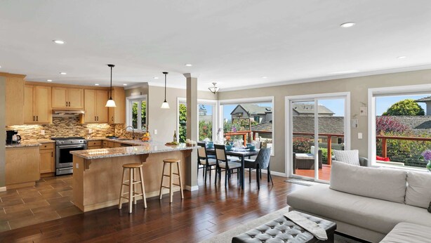 A modern kitchen with a central island, dining area with chairs, and a large sliding glass door leading to an outdoor patio. - Shell's Treasure: Fully Updated Three bedroom home with Ocean Views (Pacific Grove)