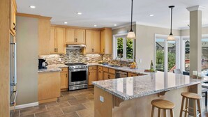 A modern kitchen with wooden cabinets, granite countertops, stainless steel appliances, and pendant lighting. - Shell's Treasure: Fully Updated Three bedroom home with Ocean Views (Pacific Grove)